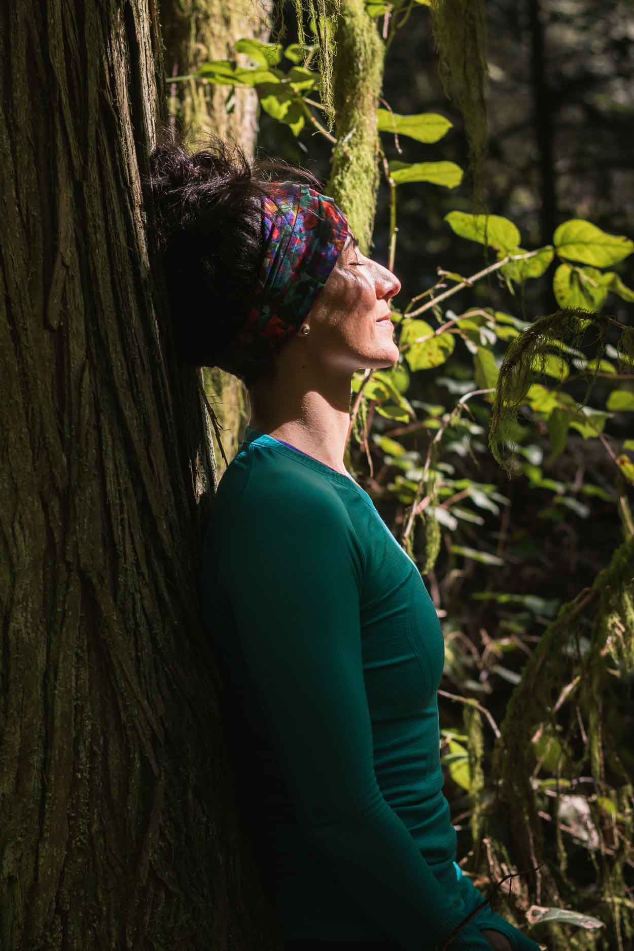 menopause woman leaning on a tree in a forest with sun rays shining on her face